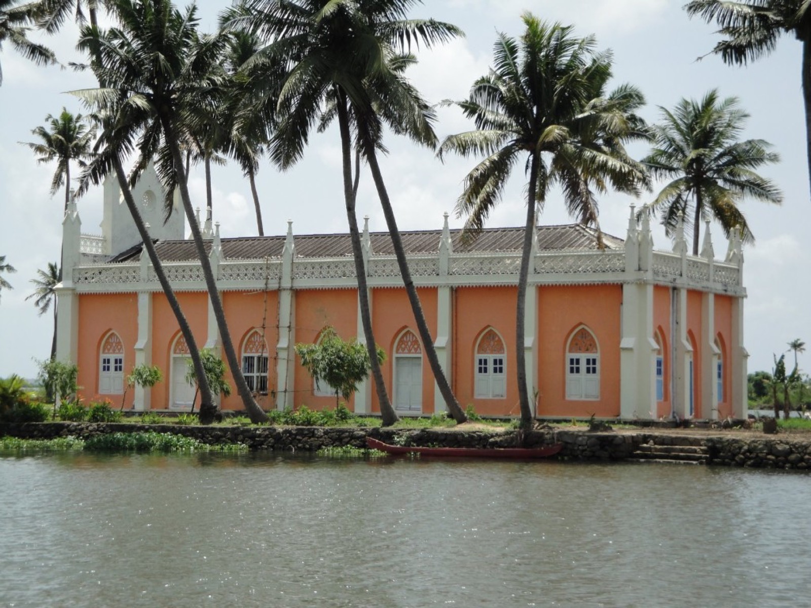 A peach-coloured church among coconut palms on the backwater
